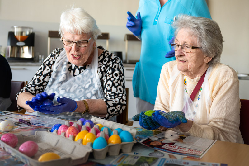Ostern in der Tagespflege. © Paul-Riebeck-Stiftung. Foto: Falk Wenzel Eine Pflegekraft hilft Senioren beim Ostereier bemalen in der Tagespflege der Paul-Riebeck-Stiftung